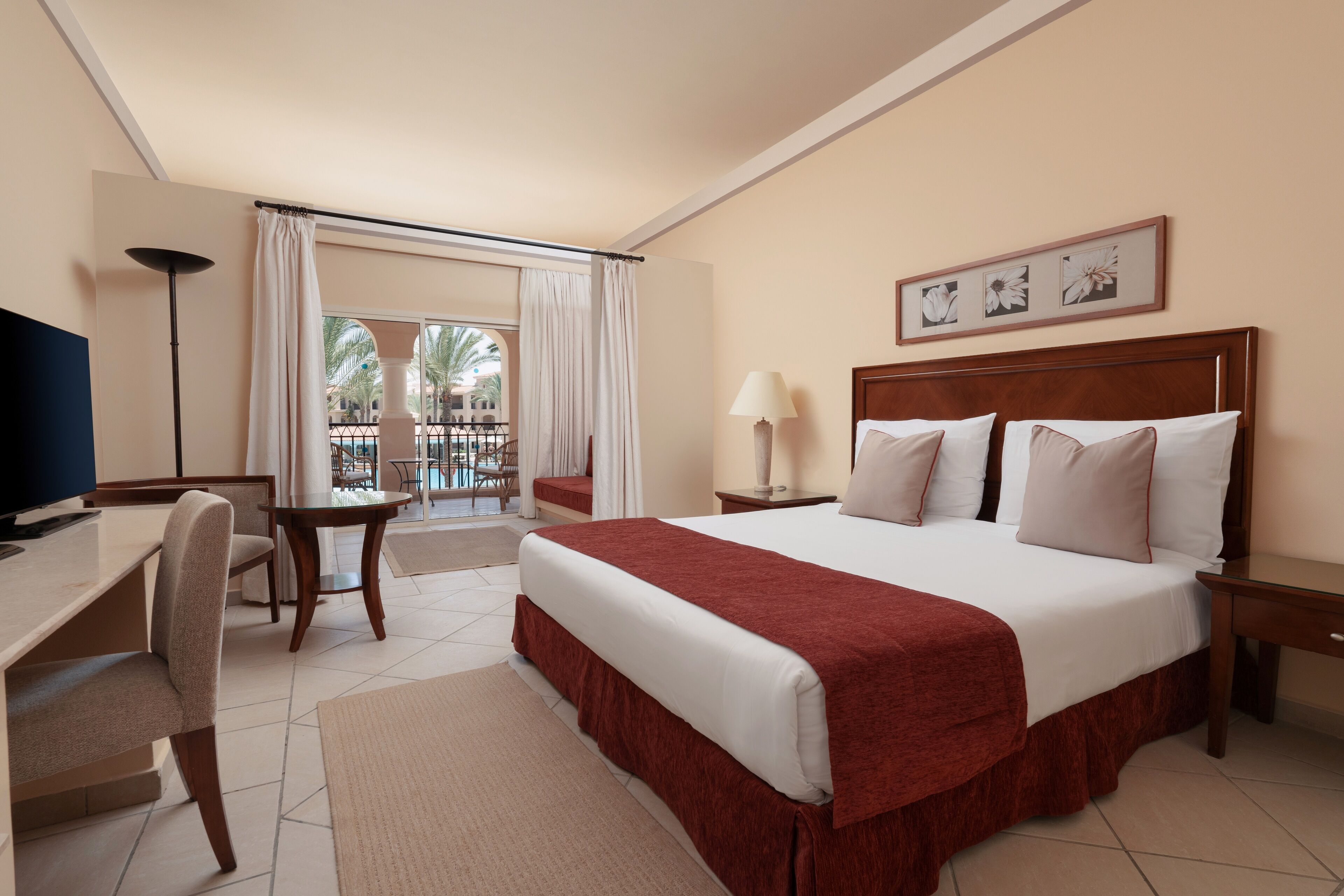 A hotel room with a large bed, a desk, a chair, a lamp, and a view of the outside.