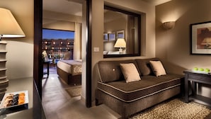A modern hotel room with a brown sofa, a small table with apples, a lamp, and a view of the cityscape through an open door. - JAZ Almaza Beach Resort, Almaza Bay (Marsa Matrouh)