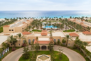 A resort with a central pool, palm trees, and a view of the ocean.