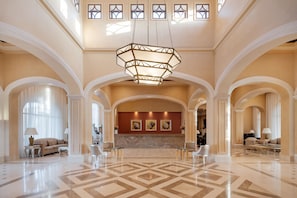 A spacious lobby with a geometric patterned floor, a central chandelier, and a reception desk.
