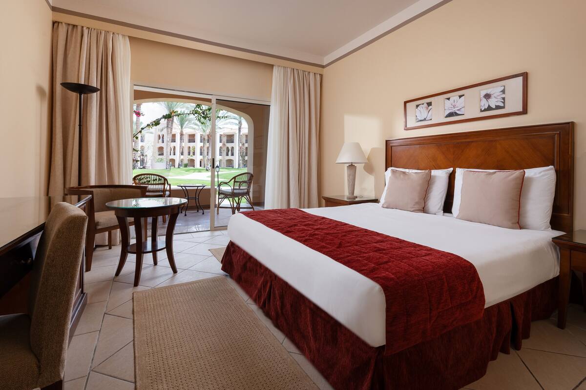 Une chambre d’hôtel avec un grand lit, un bureau, une chaise, une lampe et une vue sur une cour intérieure.