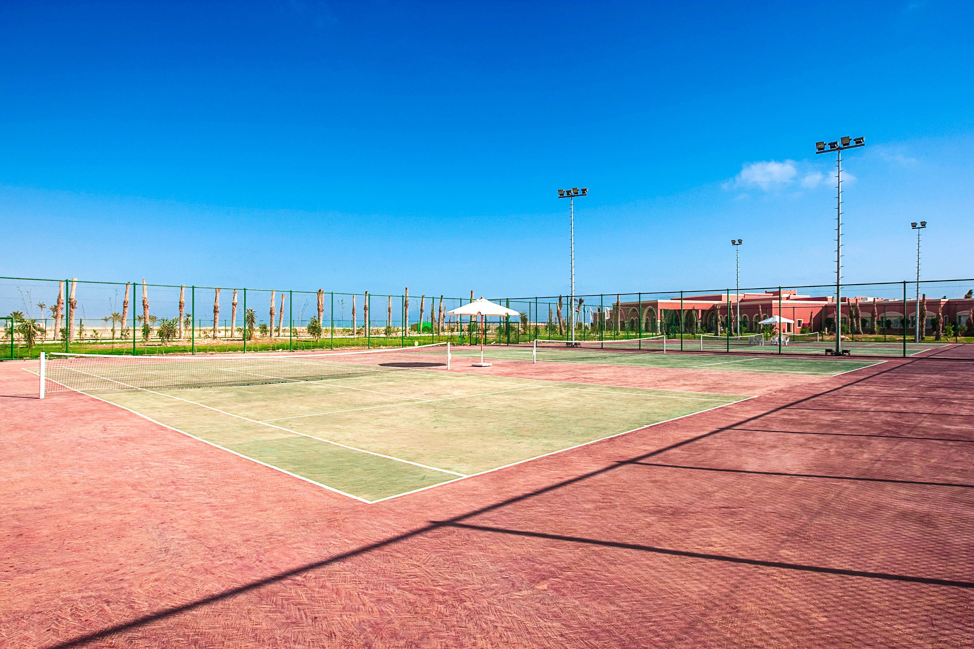Cancha de tenis exterior con red, pabellón e iluminación artificial.