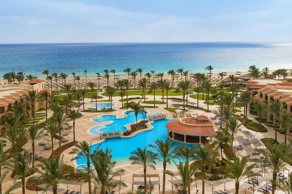 A resort with a central swimming pool, palm trees, and a beach view.