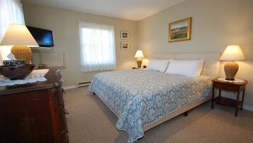 A bedroom with a bed, two bedside tables with lamps, a dresser, a television on the wall, and a window with curtains.