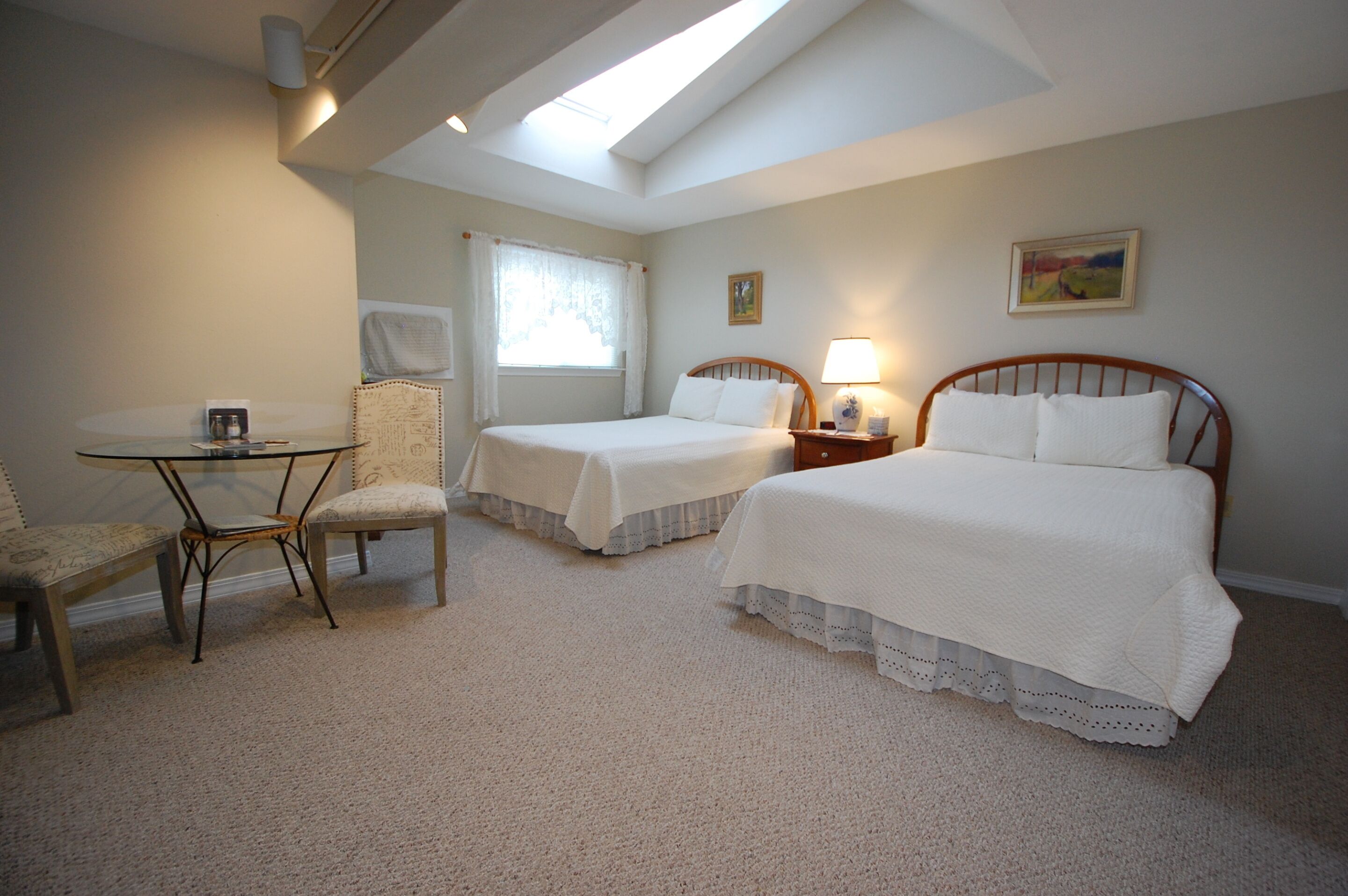 Habitación de hotel con dos camas, una mesita, una silla y una ventana con cortinas.