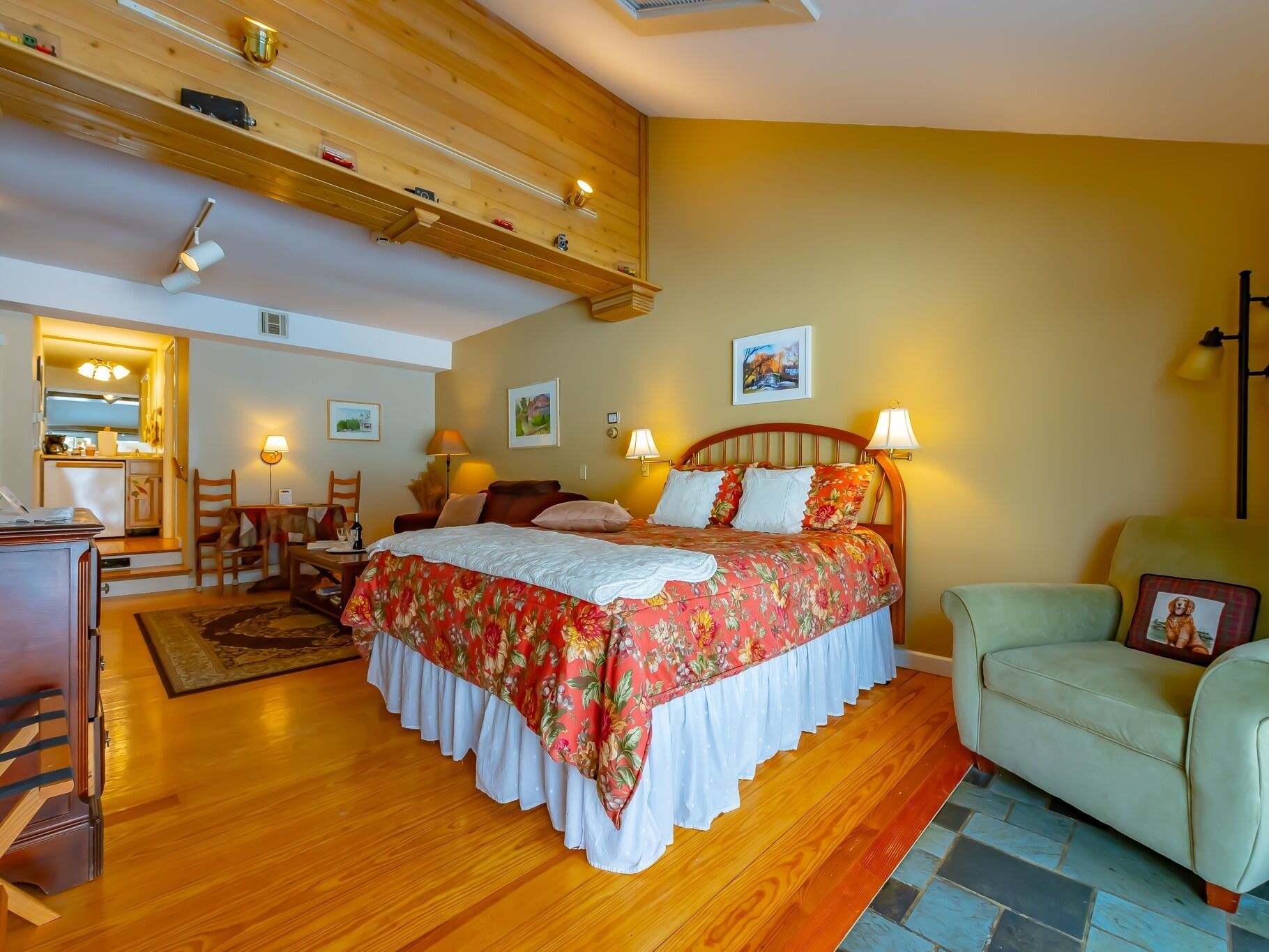 A bedroom with a wooden bed, a desk with a chair, a sofa, and a small table with a lamp.