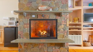 A stone fireplace with a television above it, a kitchen area to the left, and a wooden floor. - Shaker Mill Inn (West Stockbridge)
