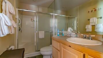 Un baño moderno con ducha envuelta en vidrio, inodoro blanco, tocador de madera con lavamanos y un espejo grande.