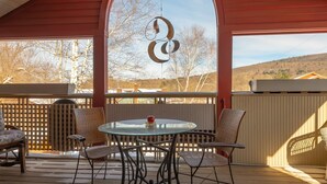 A covered patio with a round glass table and metal chairs, a wooden deck, and a view of trees and hills. - Shaker Mill Inn (West Stockbridge)