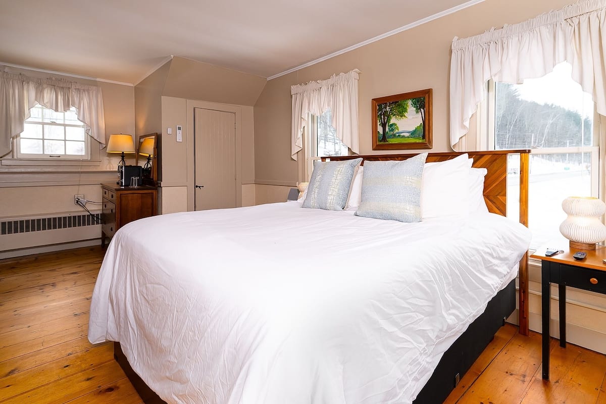 A bedroom with a large bed, a nightstand, a lamp, a dresser, and a window with curtains.