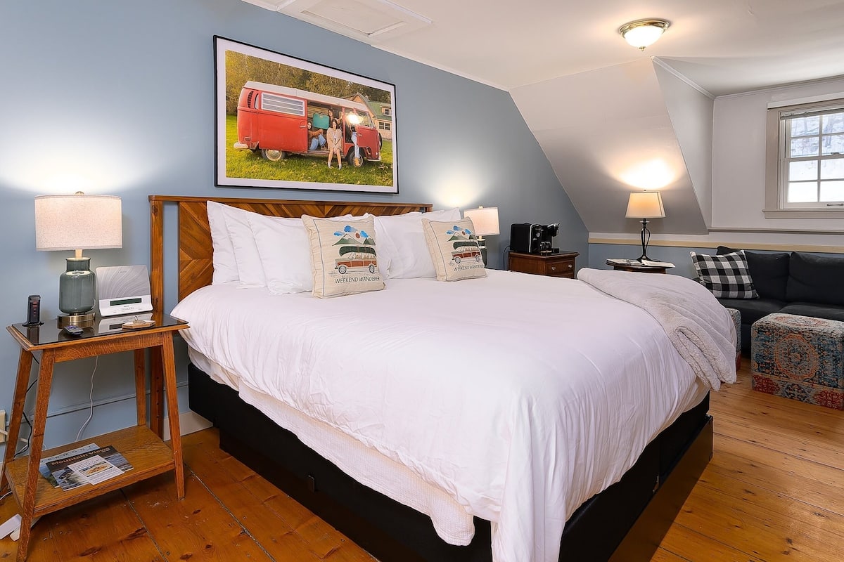 A bedroom with a large bed, two bedside tables, a nightstand, a sofa, and a window.