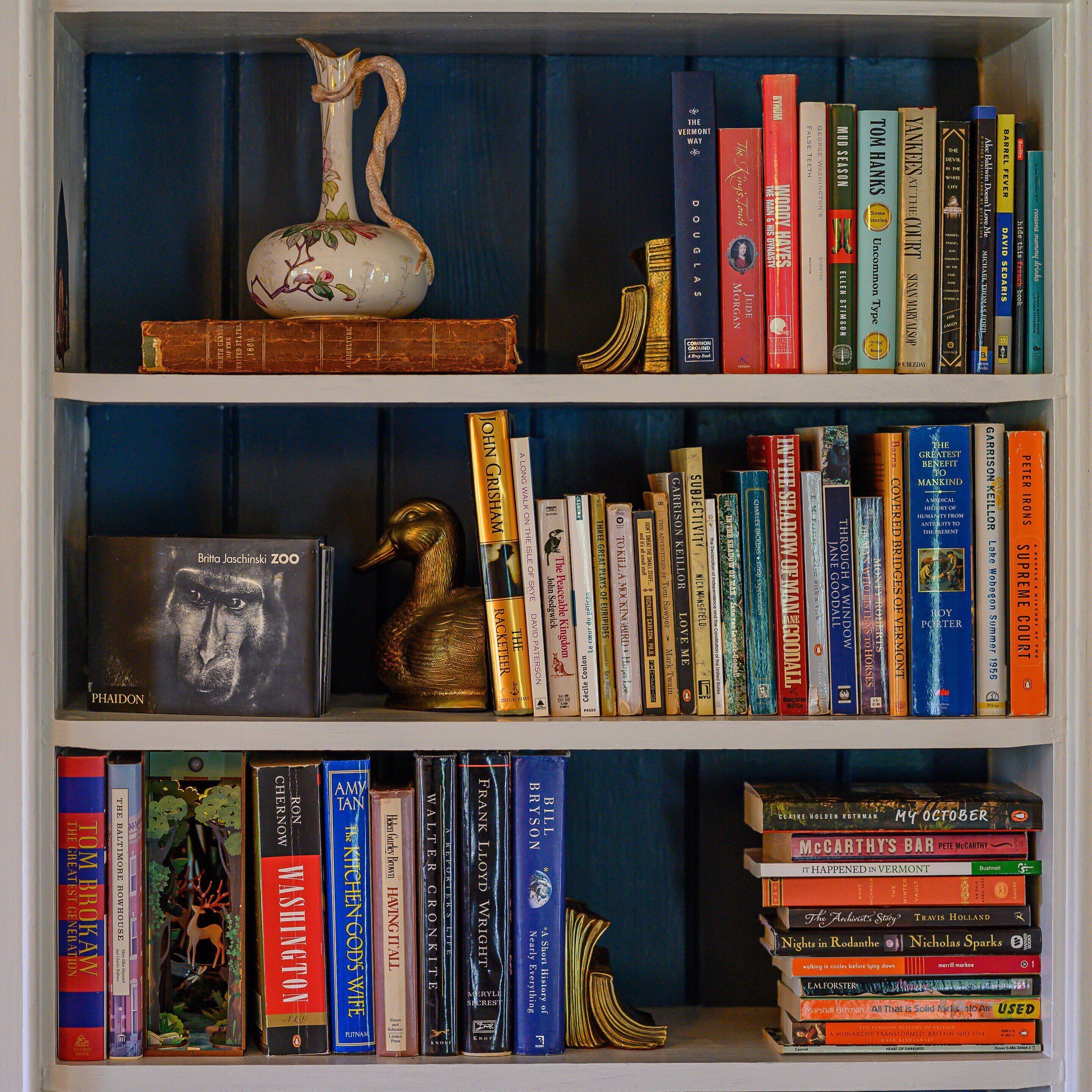A bookshelf with various books, a decorative vase, and a golden duck figurine.