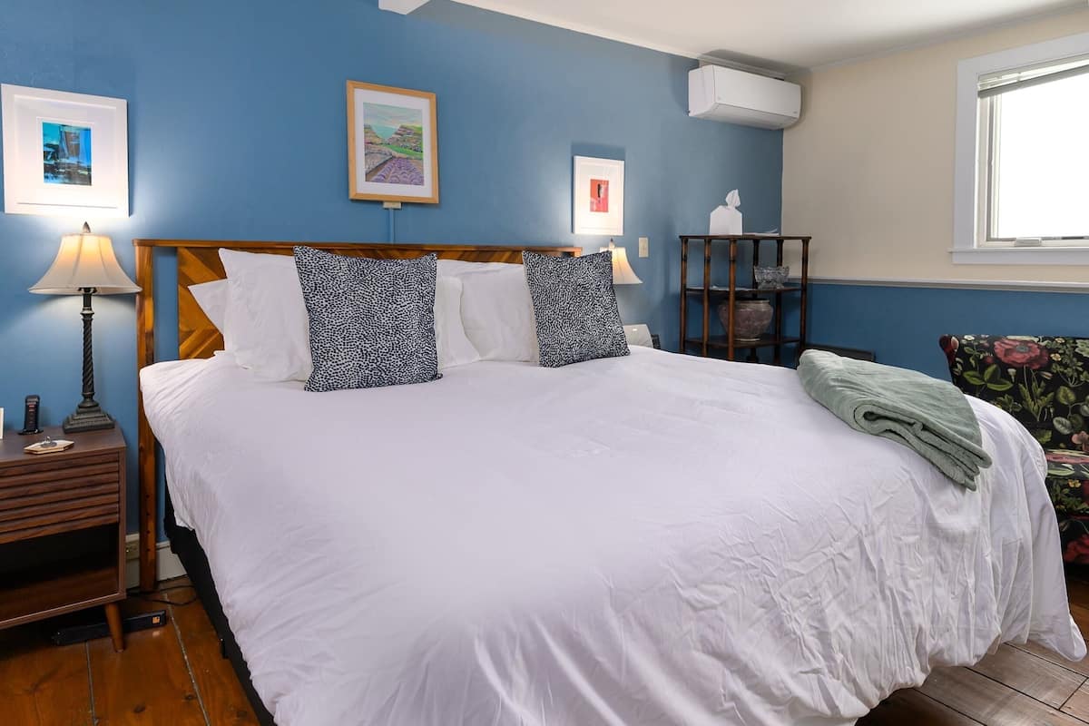 A neatly made bed with white linens and patterned pillows, a bedside lamp, and a small table with a lamp and a tissue box.