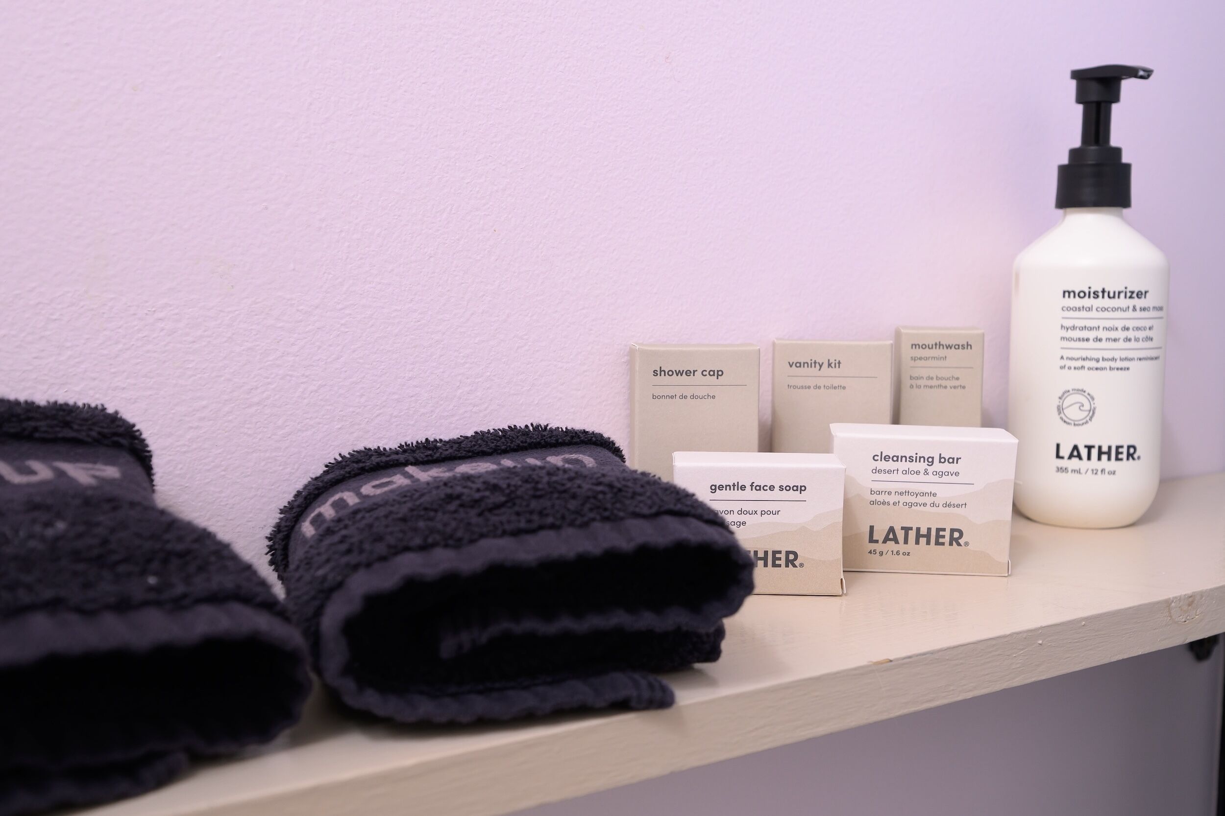 Une étagère dans la salle de bain avec des serviettes noires, un bonnet de douche, une trousse de toilette, un bain de bouche, une lotion hydratante et un savon nettoyant.