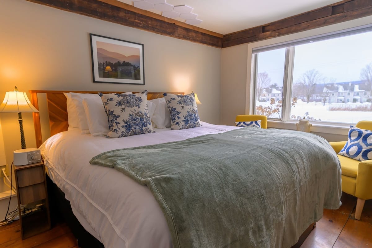 A bedroom with a large bed, a bedside lamp, a chair, and a window with a view of a snowy landscape.