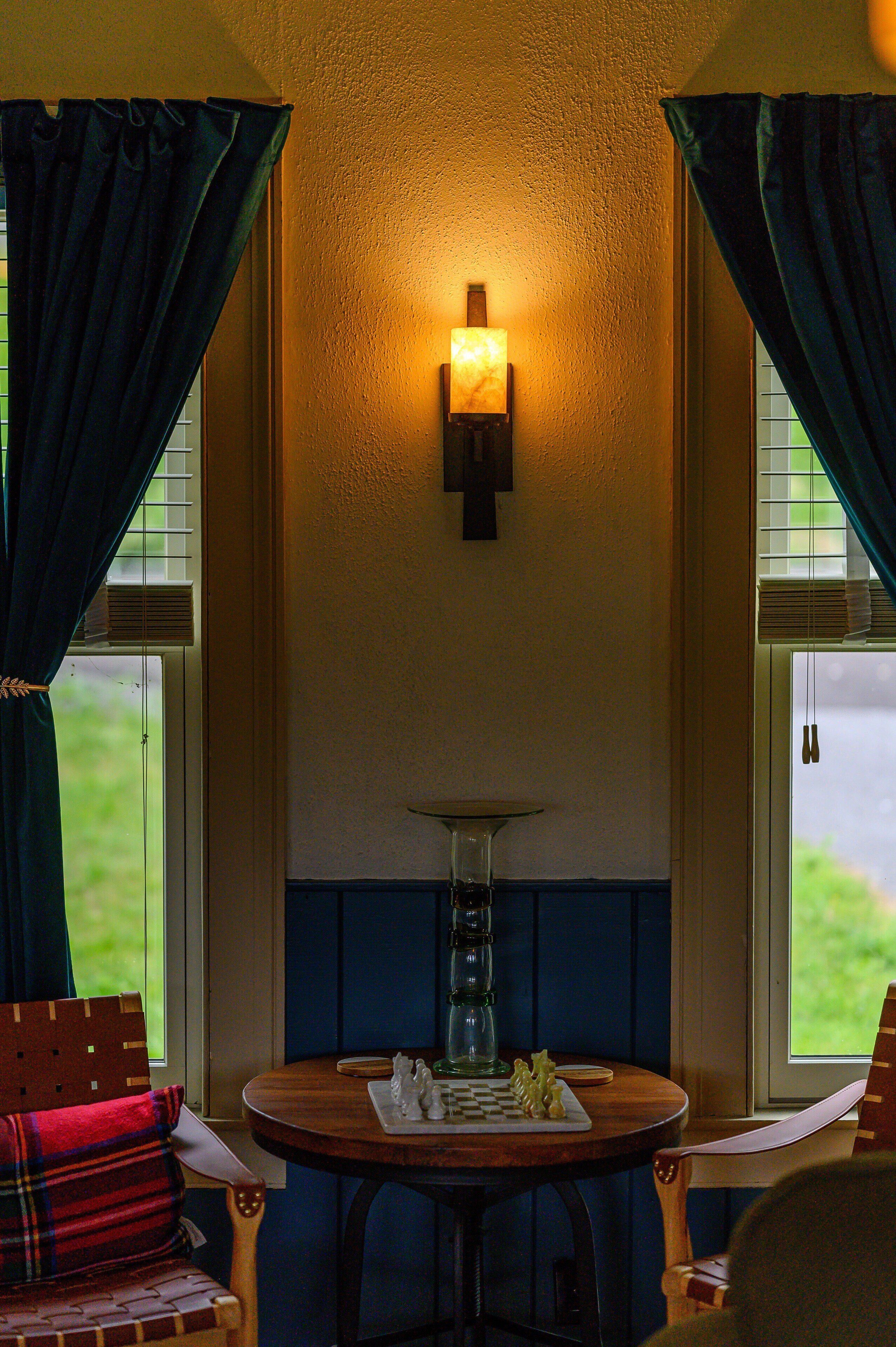A cozy room with a wooden table, a lamp, and a view of the outdoors through the window.