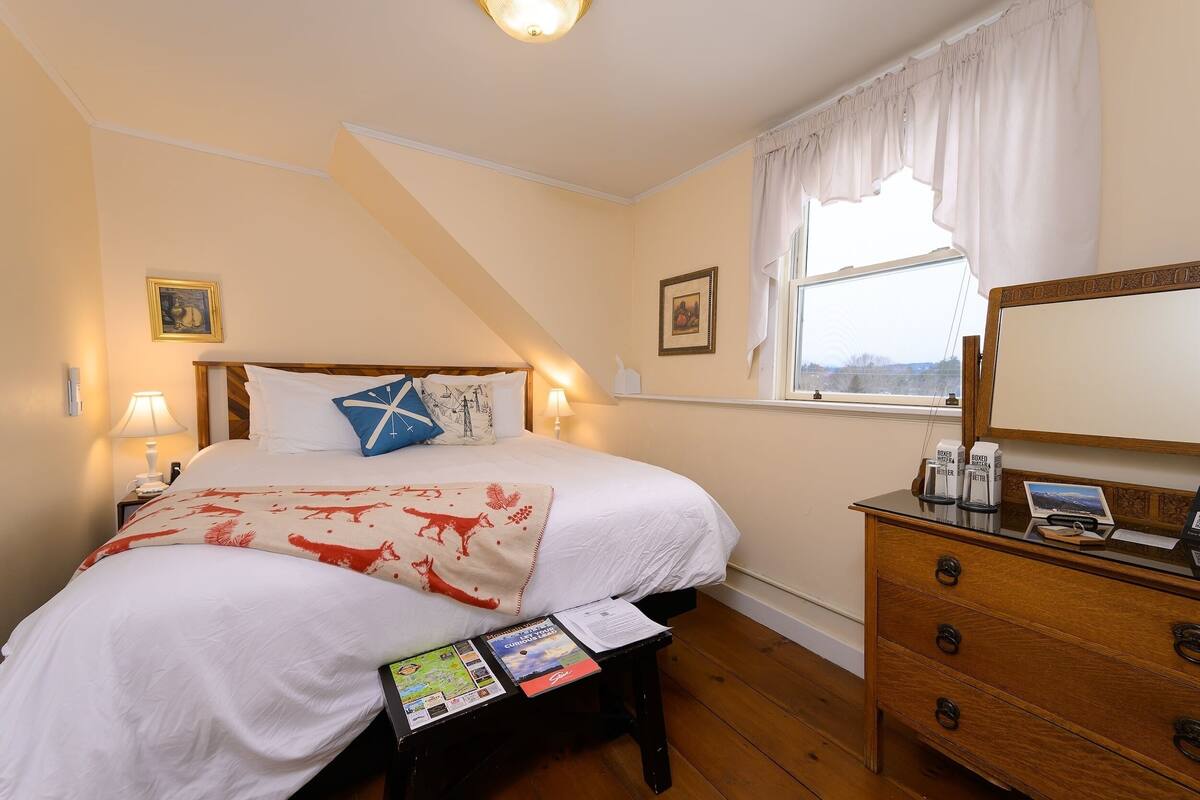 A bedroom with a bed, bedside table, dresser, and a window with curtains.