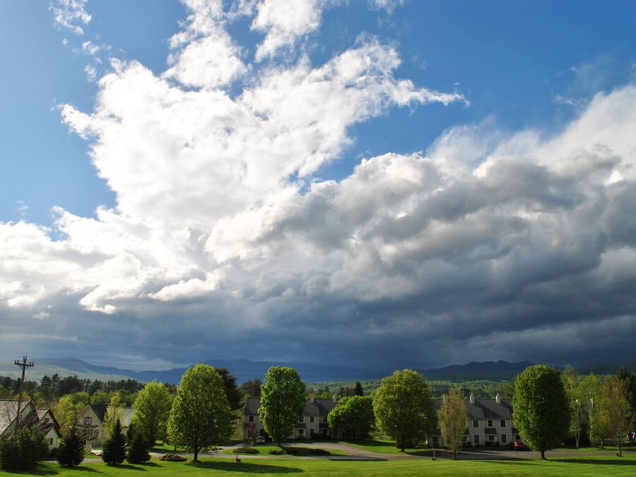 Ein Wohngebiet mit Häusern, einem gepflegten Rasen und einem wolkenübersäten Himmel.