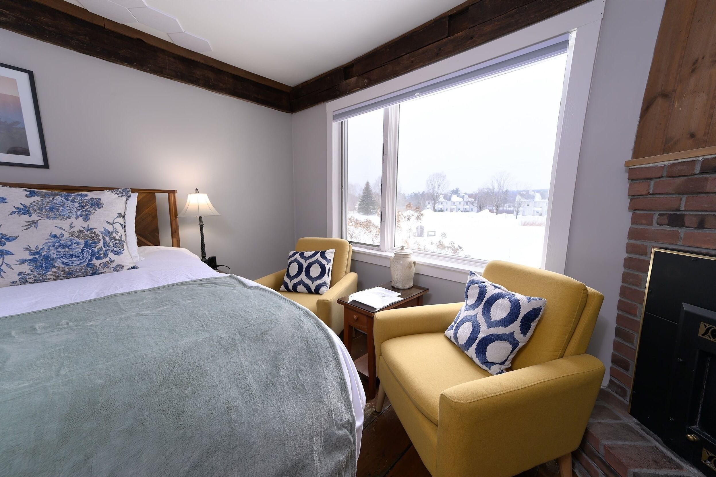 A bedroom with a bed, a yellow armchair, a window with a view of a snowy landscape, and a fireplace.