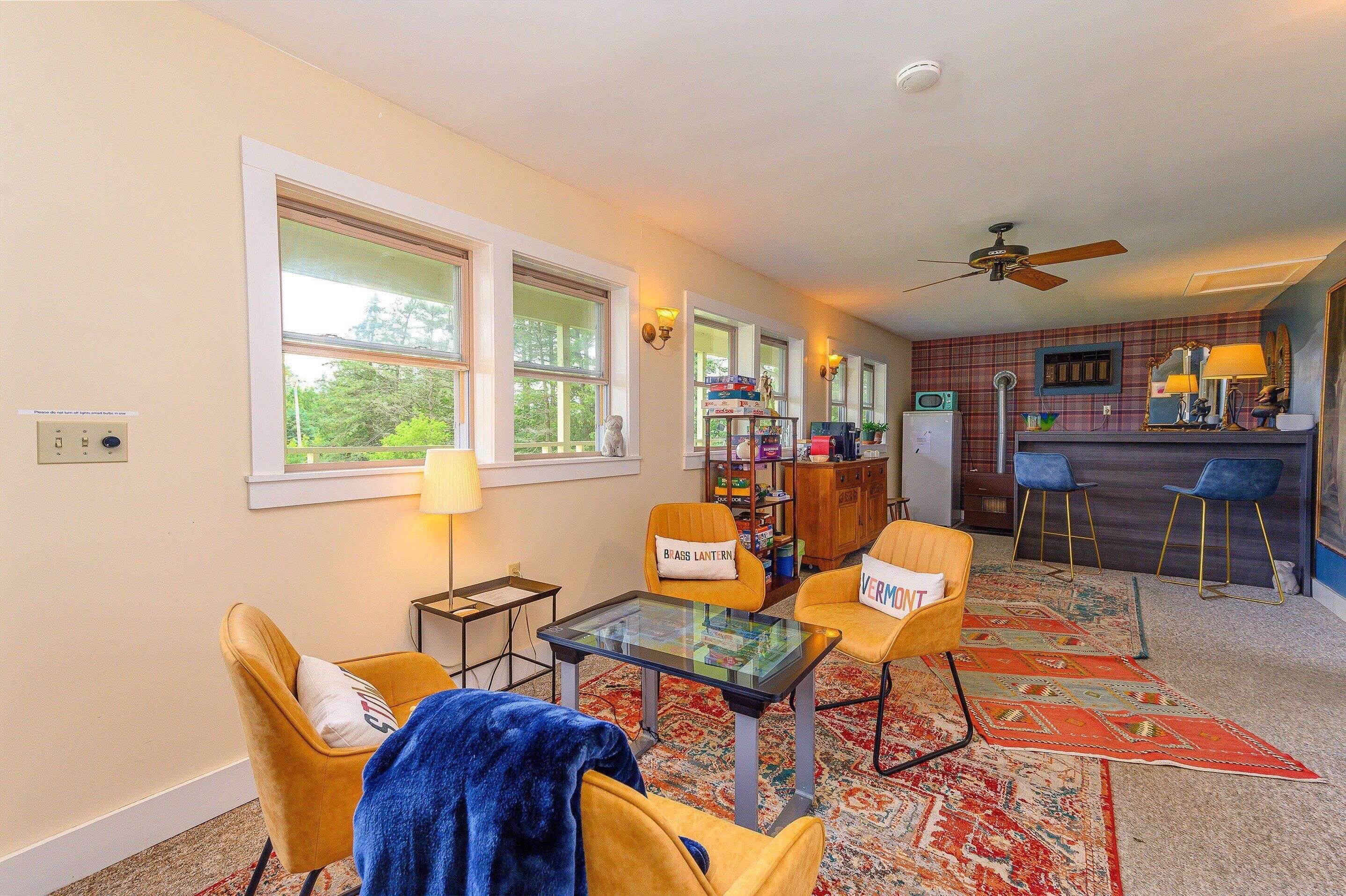 A cozy living room with a glass-top coffee table, two yellow armchairs, a blue throw blanket, and a red patterned rug.
