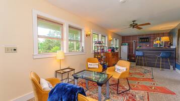 A cozy living room with a glass-top coffee table, two yellow armchairs, a blue throw blanket, and a red patterned rug.