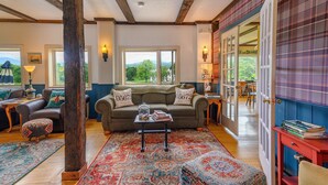 Una sala de estar acogedora con sofá, reposapiés y una mesa de centro, un ventanal con vistas, y una alfombra estampada.