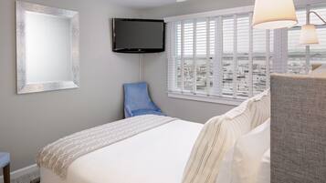 Una habitación de hotel con una cama, televisión, ventana con persianas y vista a la ciudad.