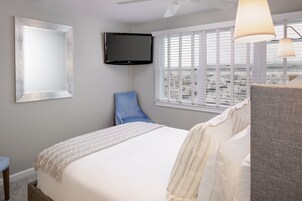 Una habitación de hotel con una cama, televisión, ventana con persianas y vista a la ciudad.