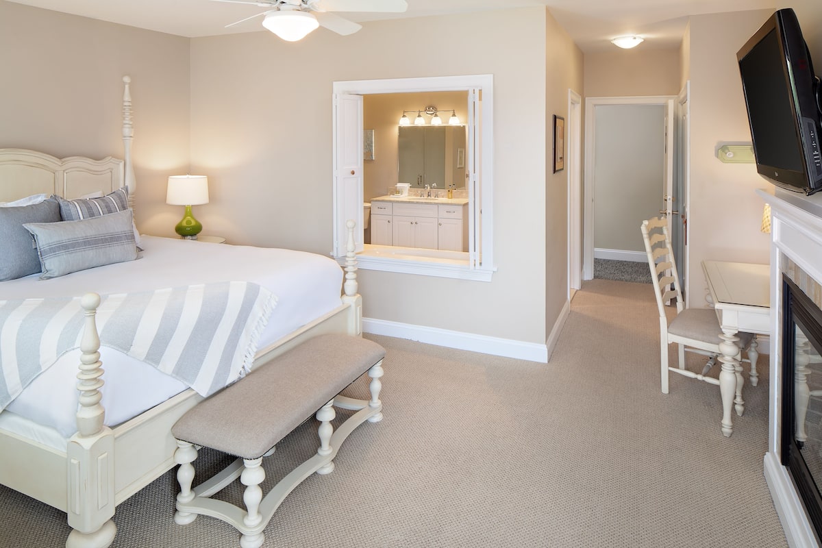 A bedroom with a bed, bedside table, lamp, and a view into the bathroom.