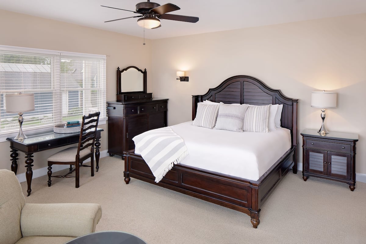 A bedroom with a large bed, a desk, a chair, a dresser, and a nightstand.
