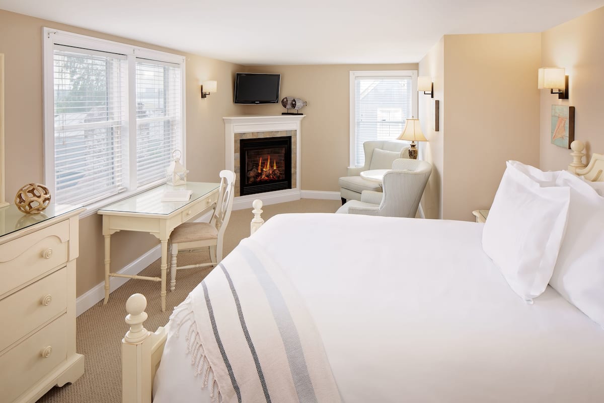 A hotel room with a bed, a desk, a chair, a fireplace, and a television.