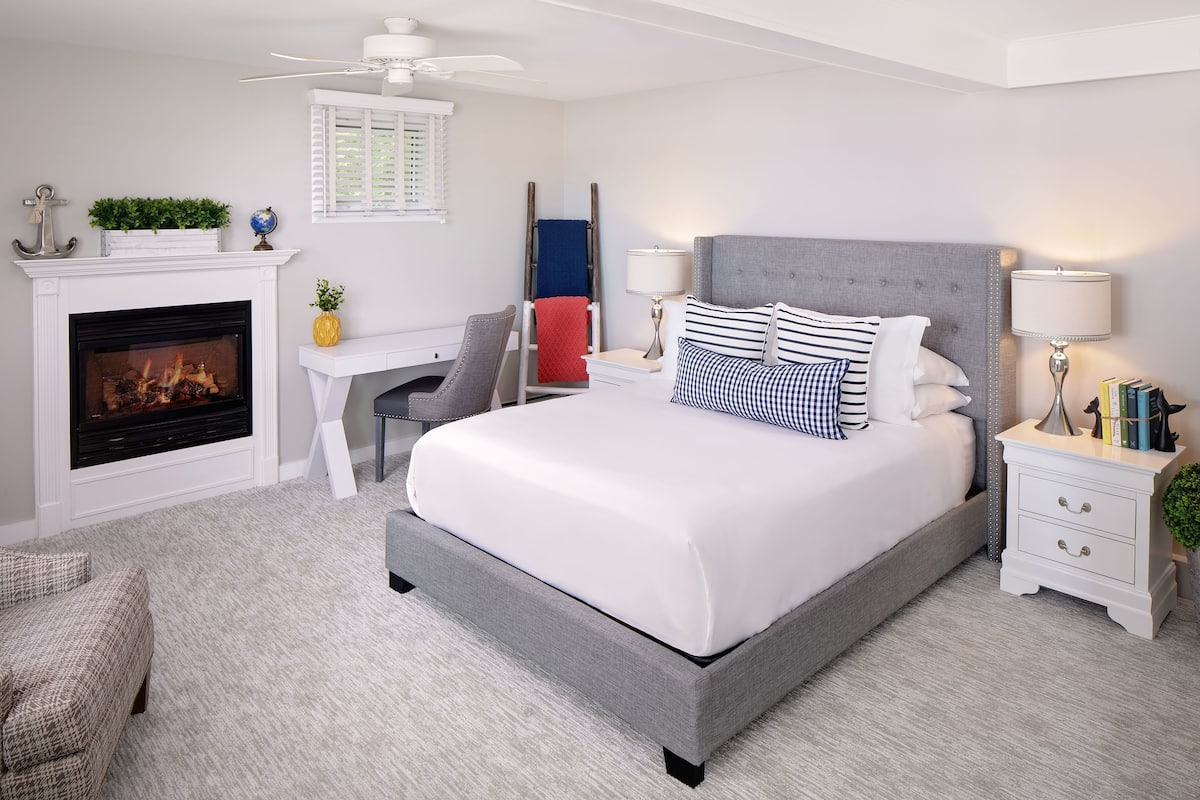 A bedroom with a large bed, a fireplace, a desk, and a chair.