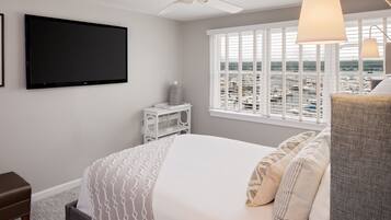 Une chambre avec un lit, une télévision, un ventilateur de plafond, une fenêtre avec des stores et une vue sur un port de plaisance.