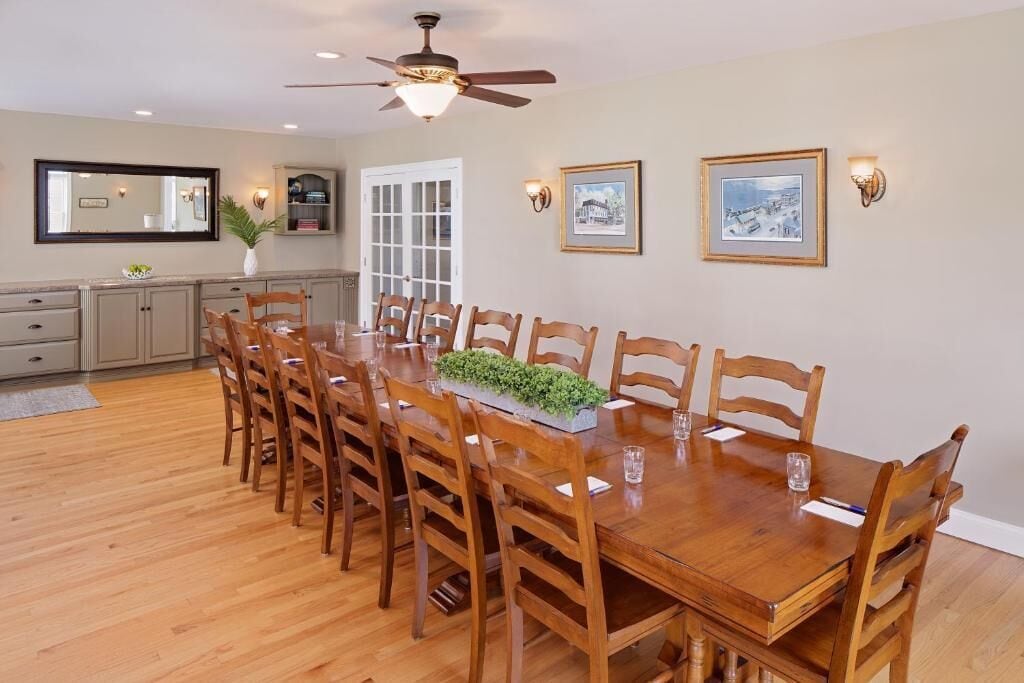 A dining room with a wooden table and chairs, a ceiling fan, and wall-mounted lights.