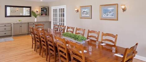 A dining room with a wooden table and chairs, a ceiling fan, and wall-mounted lights.