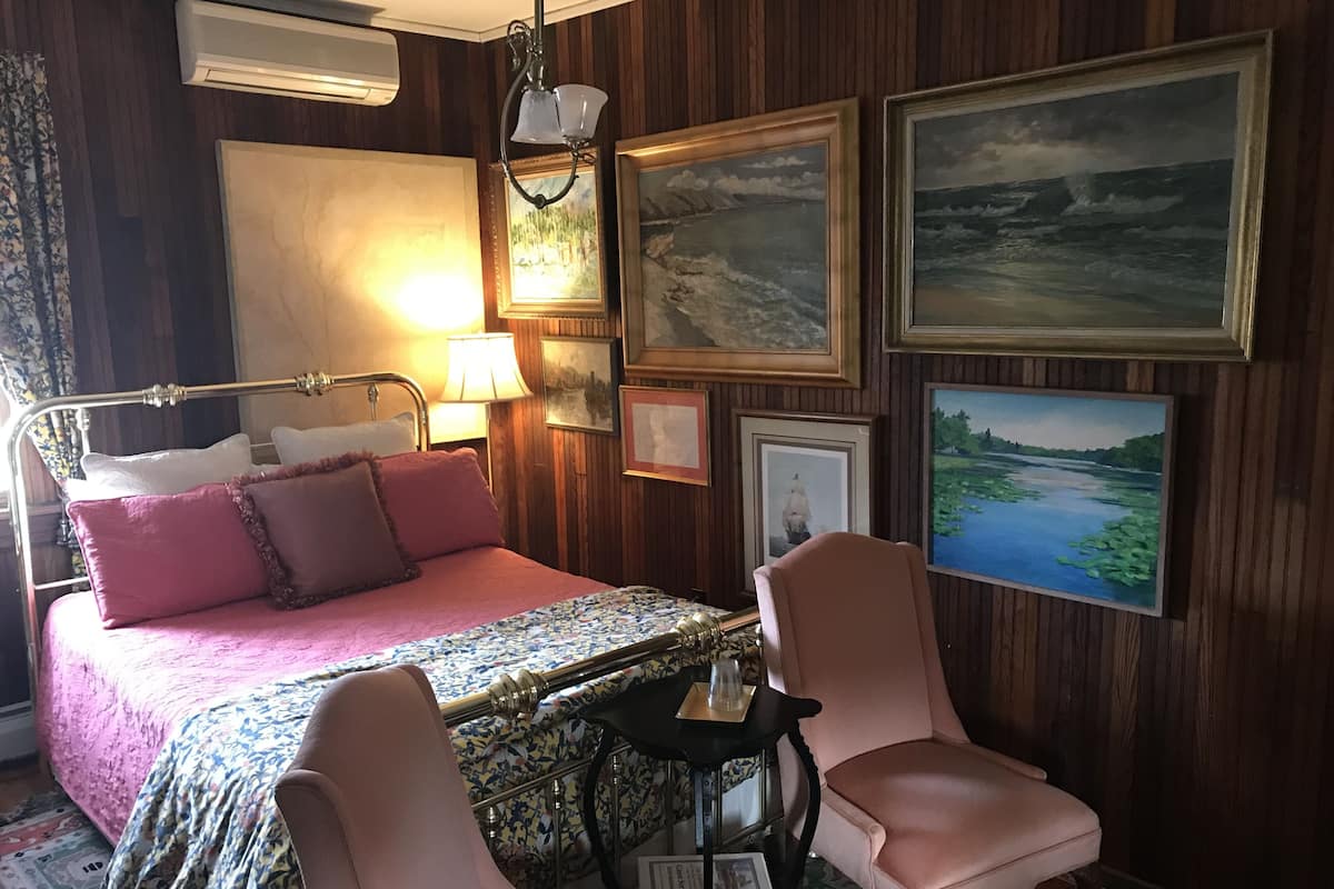 Una habitación con cama, dos sillas, una mesa y varias fotos enmarcadas en la pared.