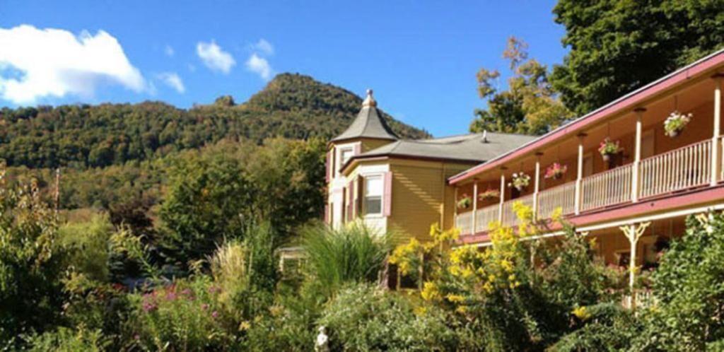 A two-story building with a balcony, surrounded by lush greenery and a mountainous backdrop.