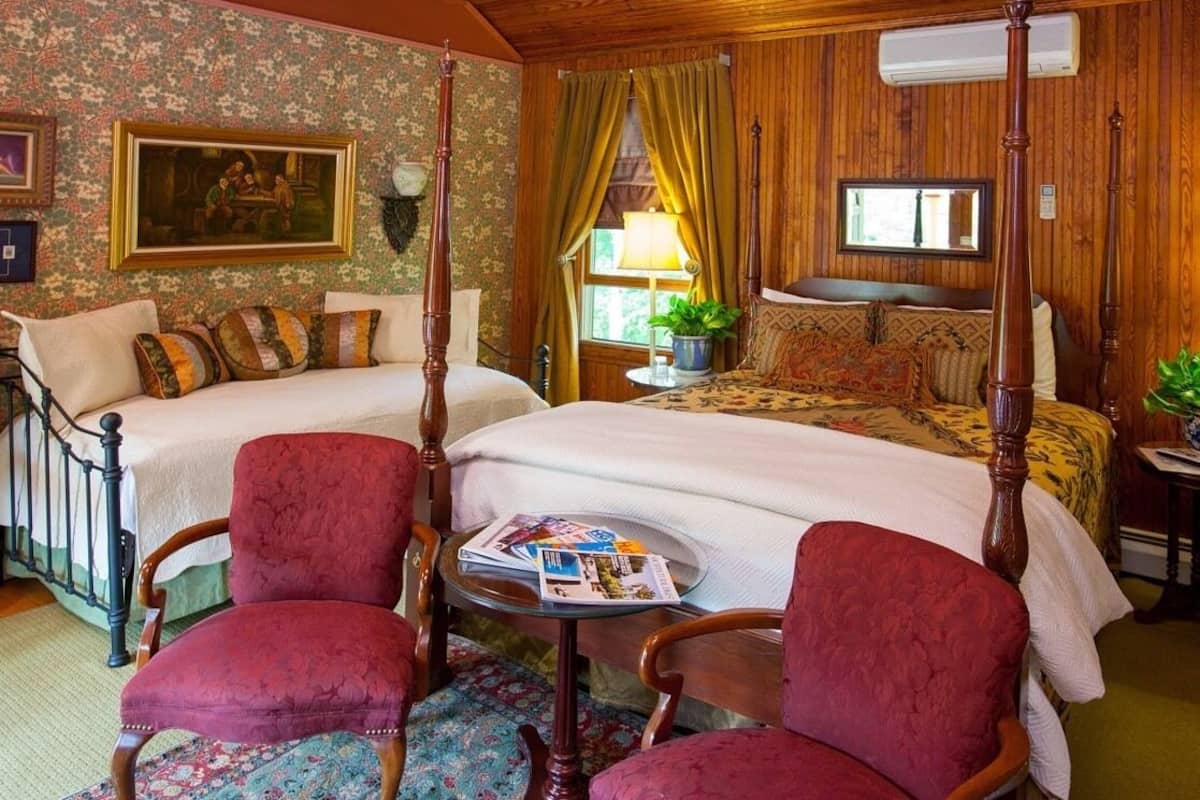 Una habitación tradicional con una cama con dosel, dos sillones, una pequeña mesa redonda con revistas y un cuadro en la pared.