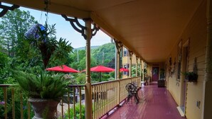 A covered porch with a red floor, potted plants, and red umbrellas. - Fairlawn Inn (Hunter)