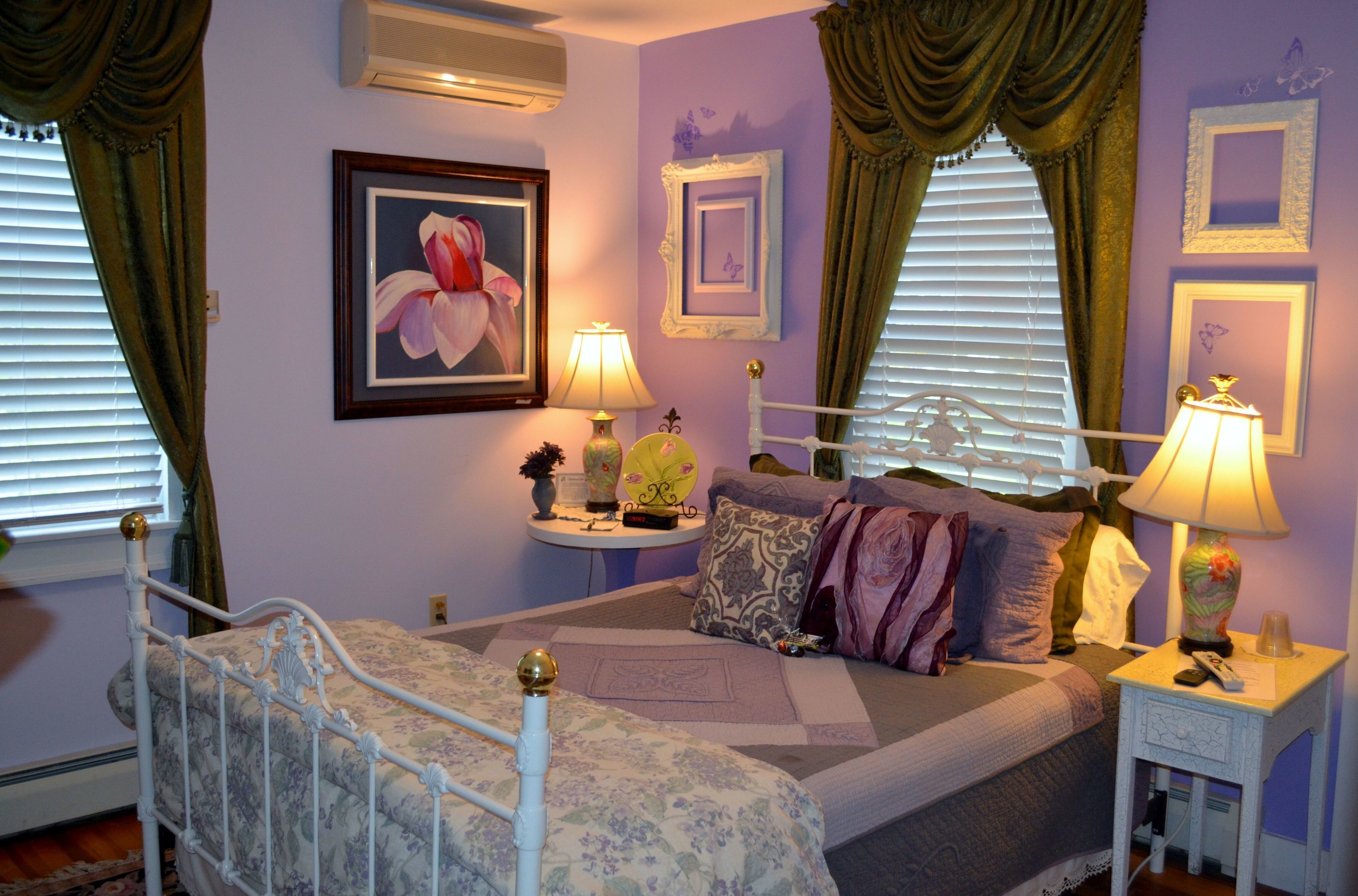 A bedroom with a bed, two bedside tables, a nightstand, a window with curtains, and a wall-mounted air conditioner.