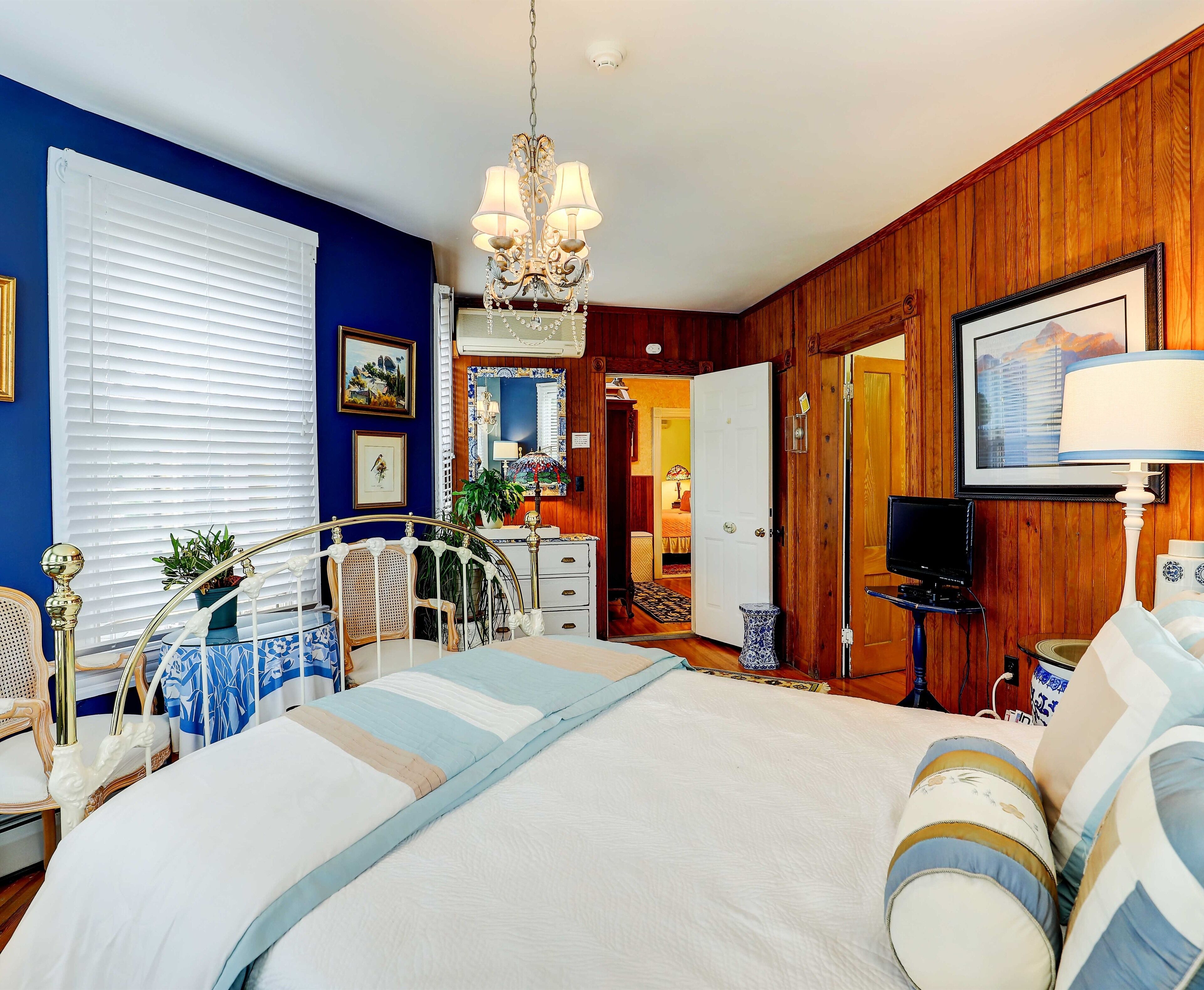 A bedroom with a bed, bedside table, TV, and a chandelier.