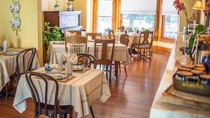 A dining area with wooden tables and chairs, a buffet counter, and a view through large windows. - Bross Hotel (Paonia)