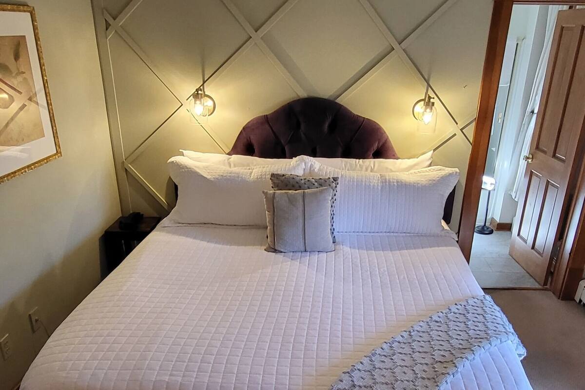 A bedroom with a bed, a ceiling fan, a patterned rug, and a wall-mounted light fixture.