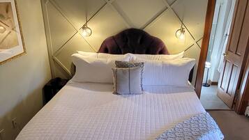 A bedroom with a bed, a ceiling fan, a patterned rug, and a wall-mounted light fixture.