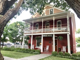 A two-story building with a balcony, labeled "BROSS HOTEL," featuring a traditional architectural style with white columns and a red brick facade.