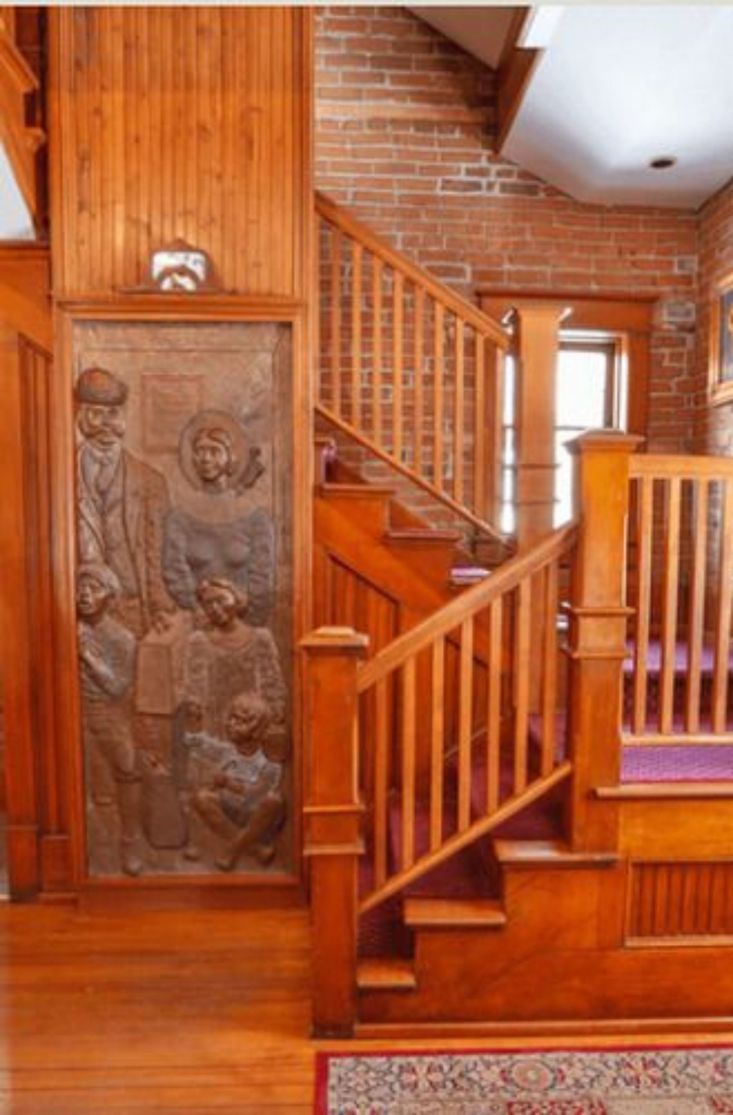 A wooden staircase with a handrail, a brick wall, and a decorative panel with figures.