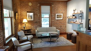 A cozy room with a brick wall, a sofa, a coffee table, and a small table with a lamp. - Bross Hotel (Paonia)
