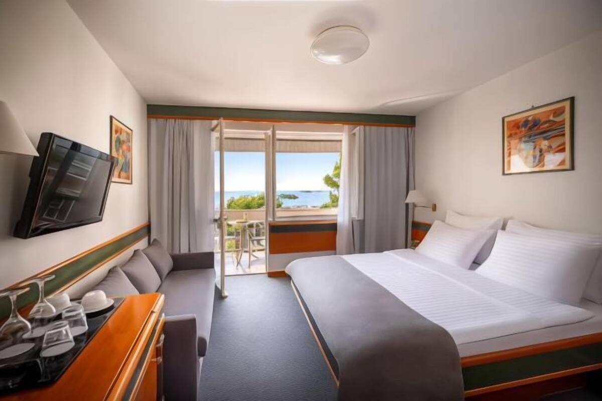 A hotel room with a bed, a desk with a computer, a TV, and a balcony with a view.