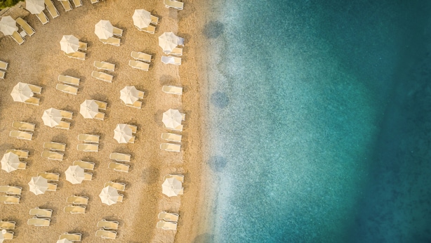 Vista aérea de una playa con filas de tumbonas y sombrillas.