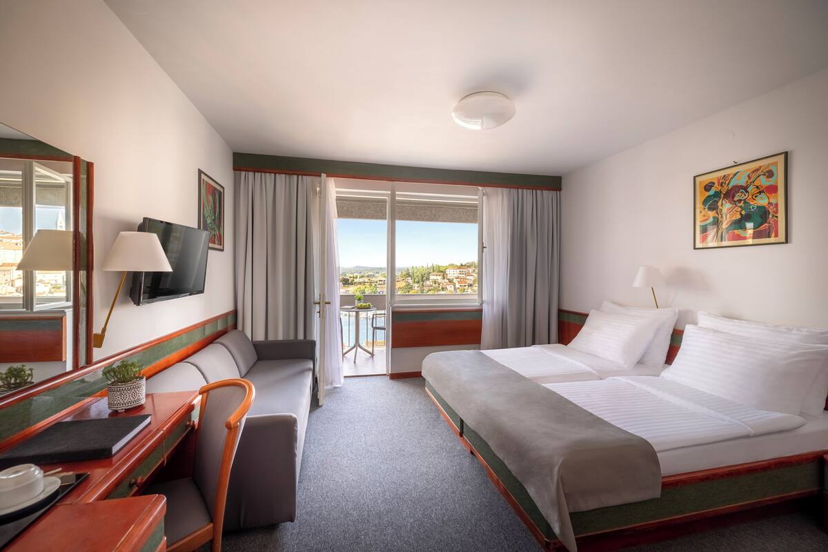 Quarto de hotel com cama, escrivaninha, cadeira, televisão e varanda com vista.